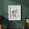 The Dill – Original Ceramic Wall Art, inspired by Irish botanical design, hangs on a dark green wall above a wooden cabinet adorned with a potted plant, stacked books, and a small landscape painting.