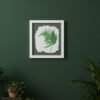 The Native Irish Fern Leaf – Original Ceramic Wall Art hangs on a dark green wall above a wooden surface with plants, books, and more greenery displayed to the right. The piece features delicately detailed fern leaves on ceramic.
