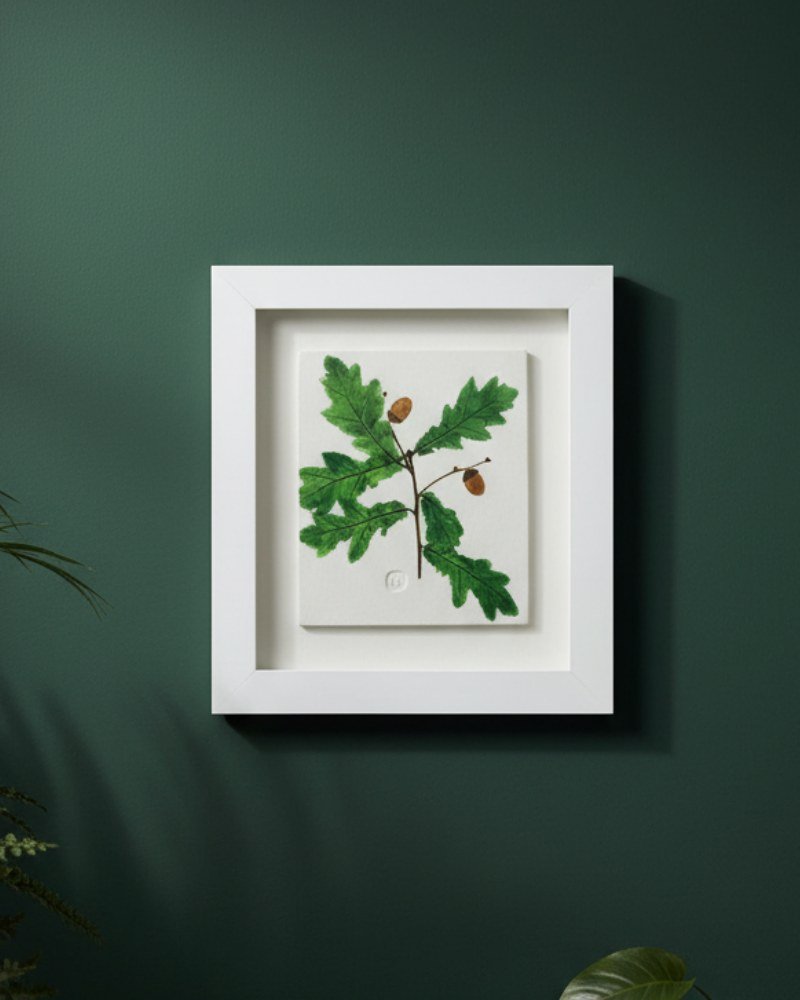 The Native Irish Fern Leaf – Original Ceramic Wall Art is showcased on a dark green wall in a white frame, with lush green plants partially visible at the edges of the image.
