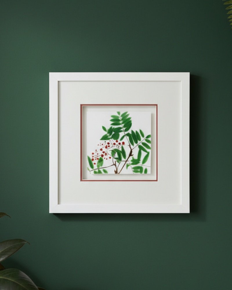 The Large Colourful Meadow Mix – Fine Art Print, featuring vibrant green leaves and red berries, hangs on a dark green wall. A white frame with double mat adds depth to this simple, modern botanical display.