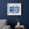 The "Wild Meadow Mix (Medium)", a framed blue botanical art print by an Irish artist, hangs on a dark blue wall above a light gray armchair with a gray blanket, next to a wooden table with books and a white vase of dried flowers.