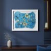 Wild Meadow Mix (Medium), a framed artwork by an Irish artist featuring blue and yellow botanical designs, hangs on a dark blue wall above a shelf with a white vase of dried grass; a mirror and part of a sofa appear in the background.