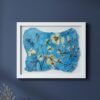 The "Wild Meadow Mix (Medium)"—a framed artwork by an Irish artist featuring a blue background, delicate yellow flowers, and black stems—hangs on a dark blue wall. A beige vase with dried stems is placed in the lower left corner.
