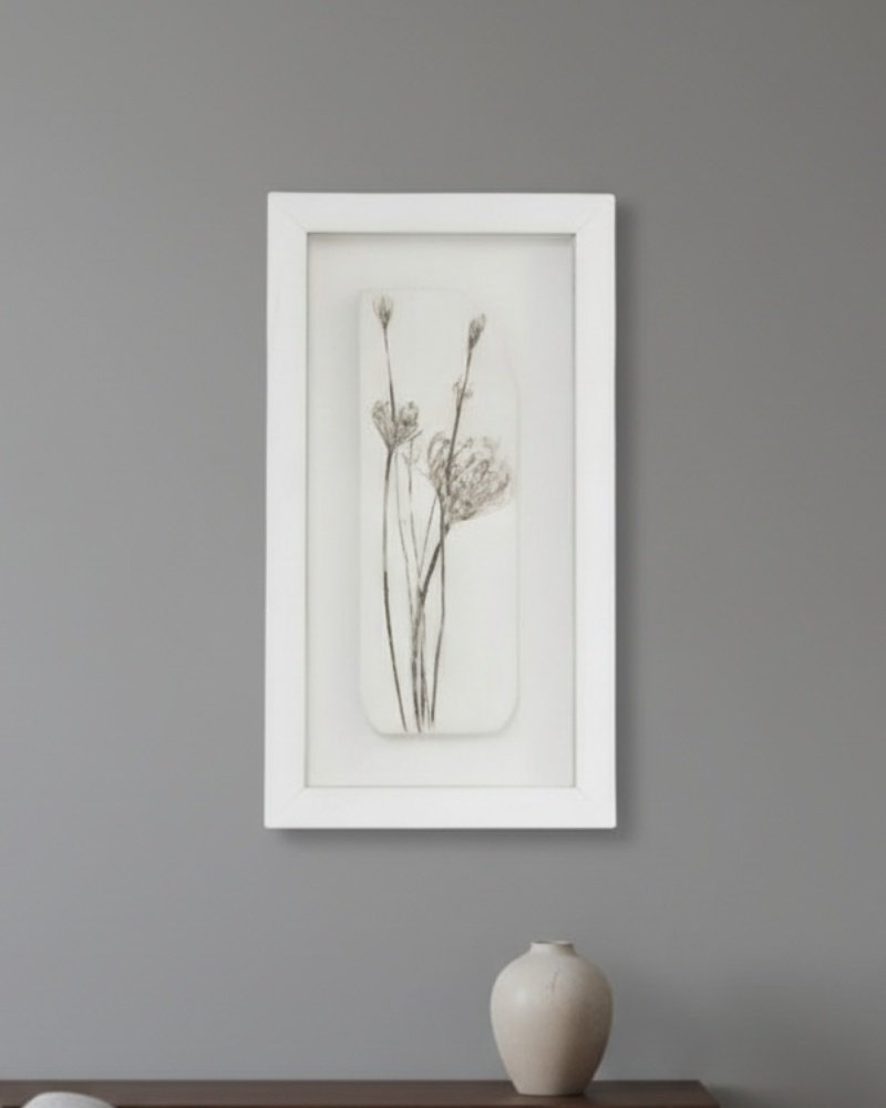 The Dill – Original Ceramic Wall Art features minimalist black botanical designs framed in white, inspired by Irish art, and is perfect for displaying on a gray wall above a wooden surface with a light beige ceramic vase.