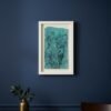 The Rosemary – Original Ceramic Wall Art, inspired by Irish design in blue and green tones, hangs on a dark blue wall above a wooden table with a gold vase of green foliage and part of a wooden chair visible.