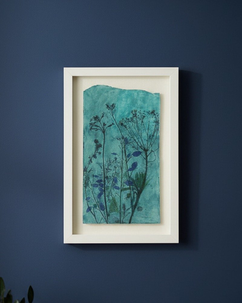 Rosemary – Original Ceramic Wall Art: A framed Irish artwork with botanical silhouettes in blue and dark green, featuring rough edges and delicate plants, displayed on a dark blue wall.