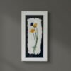 Rosemary – Original Ceramic Wall Art: Framed Irish piece with two yellow and one blue flower on white textured paper, set against a dark backdrop, displayed on a plain gray wall.