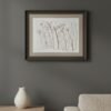 A framed fine art print titled "Serrated Wrack / Fucus Serratus" hangs on a gray wall above a light wood table with a white ceramic vase; the edge of a beige textured sofa appears on the right.