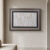 A framed print of “Coastal Seedheads” hangs on a light beige wall above a curved, light-colored chair in a minimalist room with wood flooring.