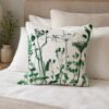 A neatly made bed with beige and white linens features the Botanical Meadow Cushion in Green, adorned with vibrant botanical prints, placed next to a vase of greenery on a wooden nightstand.